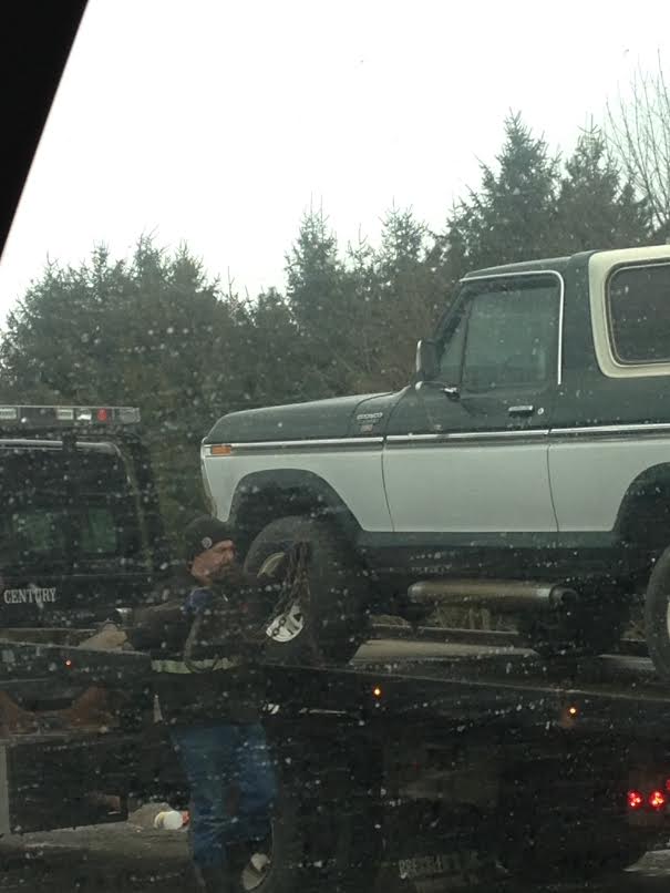 Dark green and white Ford Bronco on a tow truck with a person securing it.