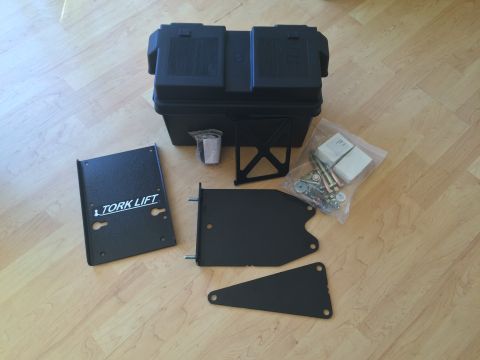 1997 Dodge 3500 - A black battery box and associated mounting hardware and plates are laid out on a wooden floor. One of the plates has "TORK LIFT" printed o…