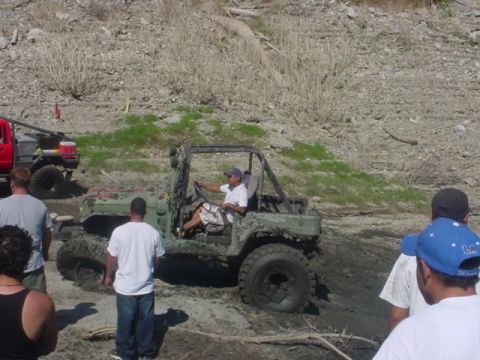 1988 Ford Bronco - A muddy Jeep Wrangler is stuck in the dirt while onlookers observe the scene.