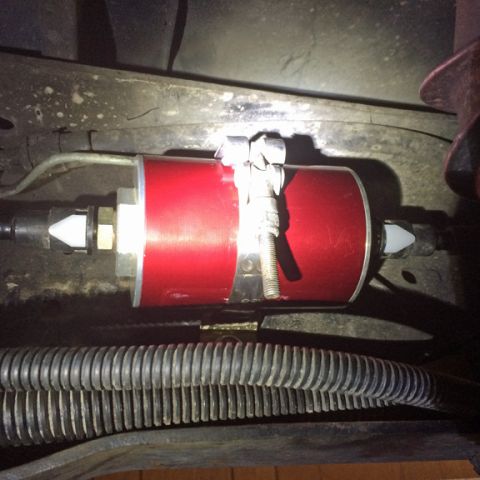 1990 Ford Bronco - A red anodized aluminum fuel filter is mounted with a clamp to the underside of a vehicle. A ribbed black hose runs below the fuel filter.