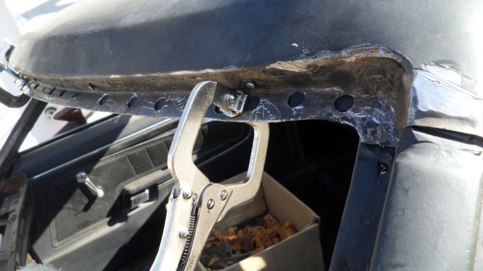 Close-up of rusted vehicle roof edge held by clamp, with interior door panel visible.