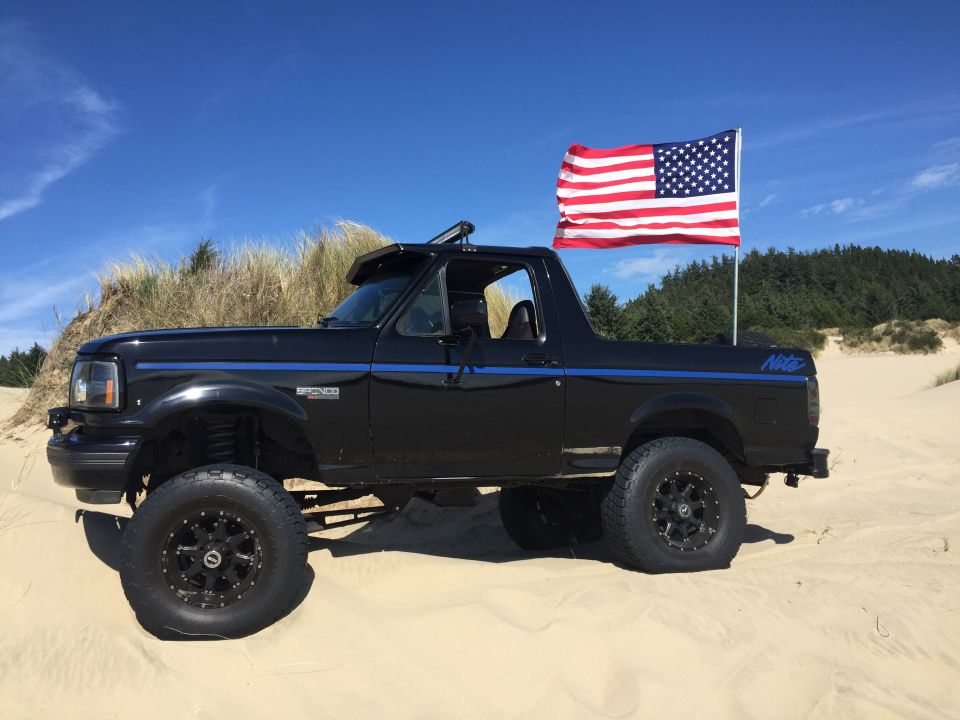 Lifted black Ford Bronco with American flag on a sand dune.