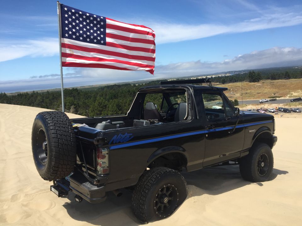 Black Ford Bronco with American flag on sand dunes, spare tire on tailgate