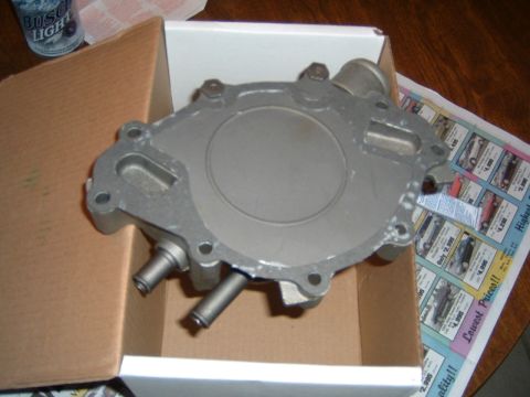 1987 Ford Bronco - A water pump part is shown inside a cardboard box with a newspaper in the background.