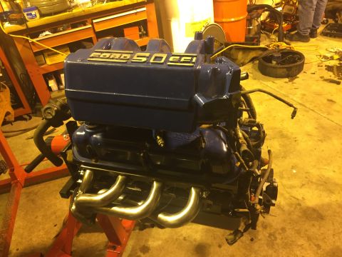 1992 Ford Bronco - A blue Ford 5.0 EFI engine is mounted on a red engine stand in a workshop. The engine features chrome headers and visible wiring harnesses.