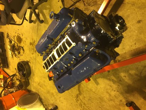 1992 Ford Bronco - A freshly painted blue V8 engine is mounted on a red engine stand in a garage. The engine features chrome valve covers and a black intake m…
