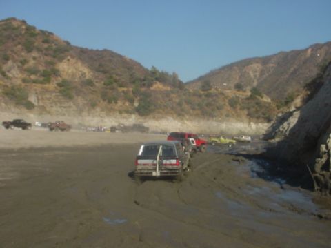 1988 Ford Bronco - Multiple vehicles navigate a muddy terrain under a clear blue sky.