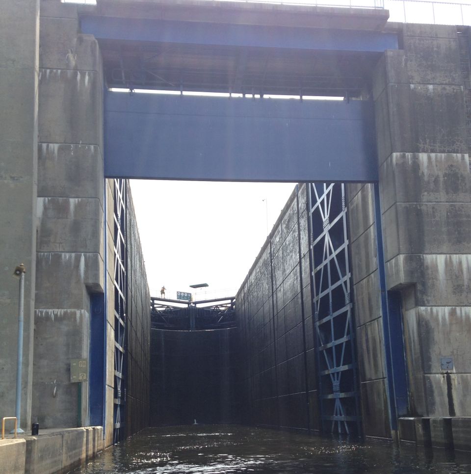 Concrete lock and dam system with a large blue gate, viewed from the water.