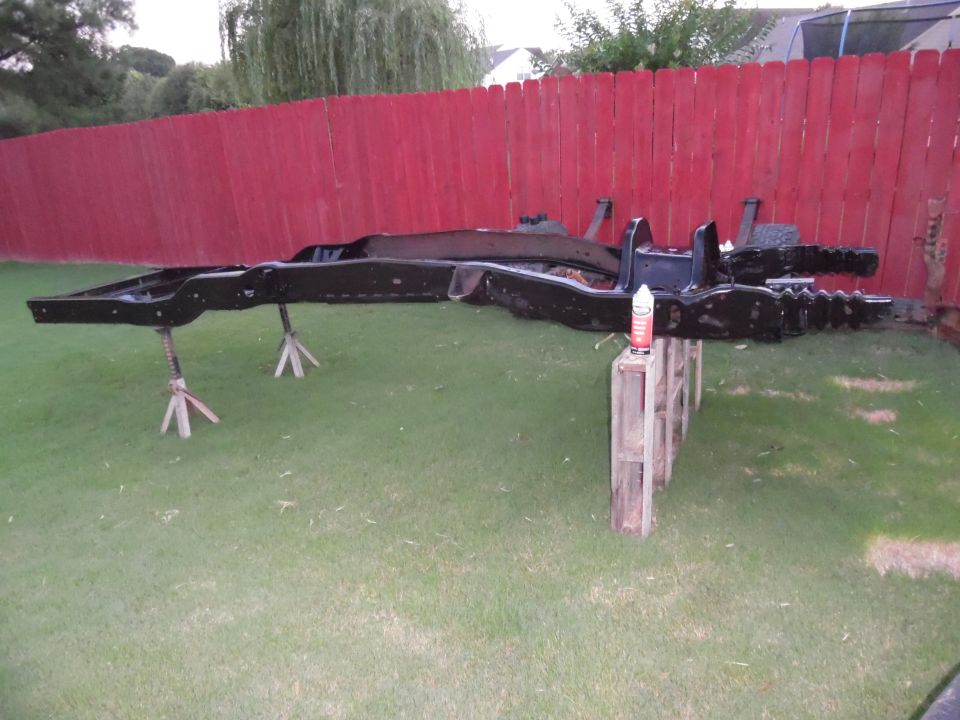 Bare black-painted truck ladder frame on jack stands in a backyard