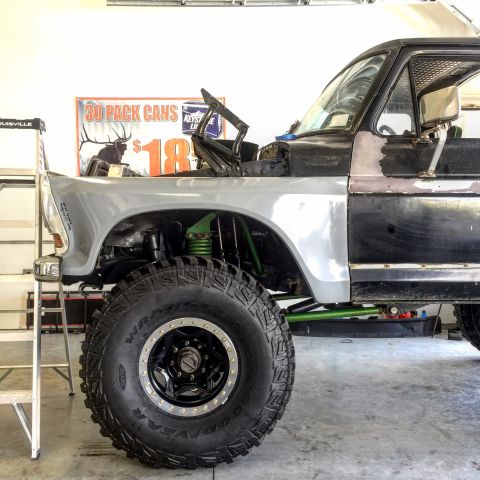 1979 Ford Bronco - Front corner of a lifted 1970s-80s Ford truck mid-build in a garage, silver fender resting loose over the exposed suspension so the green-p…