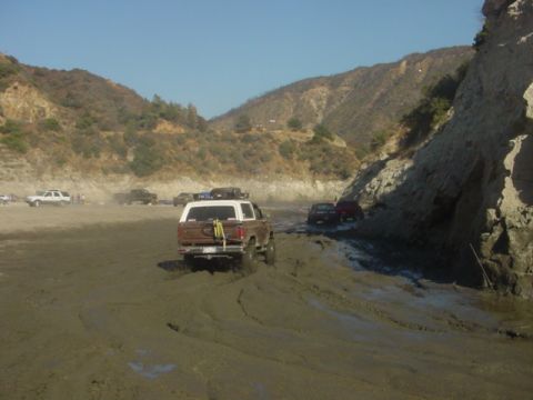 1988 Ford Bronco - Several vehicles navigate a muddy terrain, with a 1988 Ford Bronco leading the way.