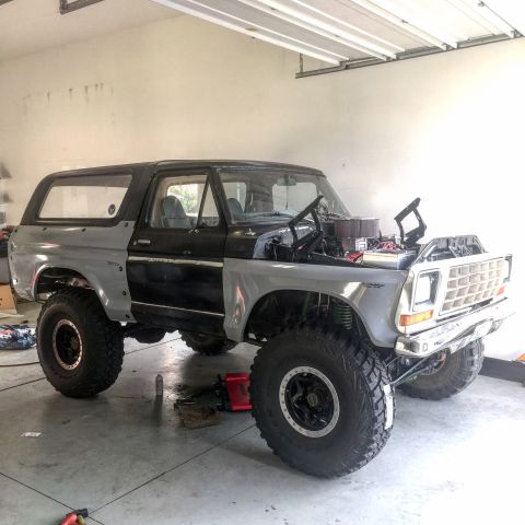 1979 Ford Bronco - Three-quarter front view of a silver and black full-size Ford Bronco mid-build in a garage, hood removed to expose a chrome round air clean…