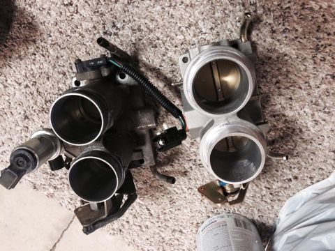 1995 Ford Bronco - Two throttle bodies are shown on a textured carpeted surface. The throttle body on the left has a black sensor attached, and the one on the…