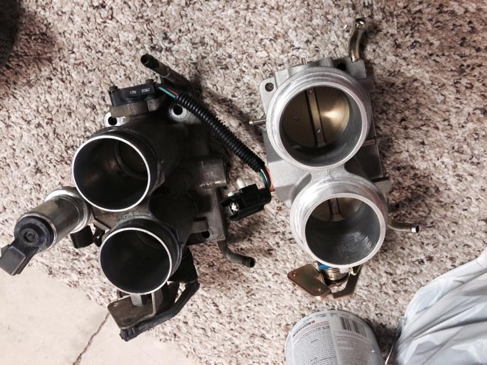 Two automotive throttle bodies on a carpeted surface.
