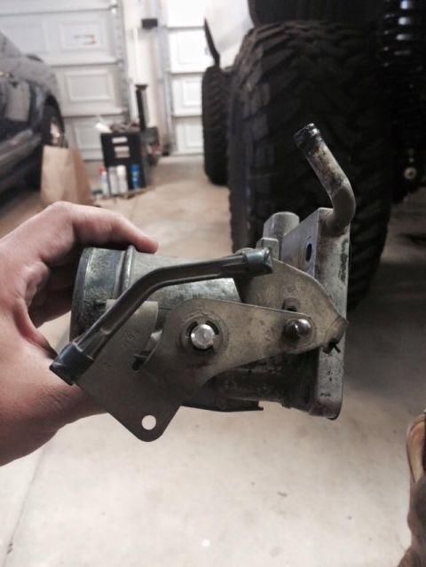 1995 Ford Bronco - A hand holds a dirty, metallic automotive part with visible linkages and a bent metal tube. The part appears to be part of an engine or exh…