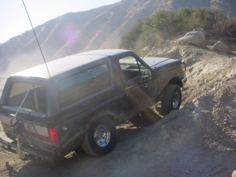 1988 Ford Bronco - This Ford Bronco is navigating a steep, dusty off-road trail with a rocky incline.