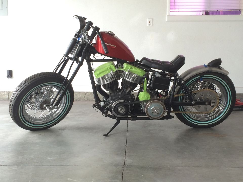 Custom motorcycle with red fuel tank and green engine covers, parked indoors
