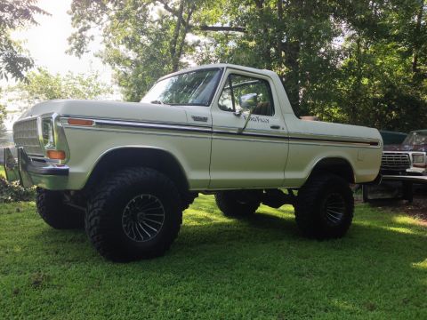 1979 Ford Bronco - A lifted white Ford Bronco with custom wheels sits on a grassy lawn under trees.