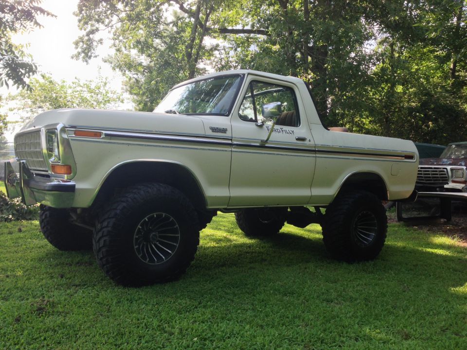 White lifted Ford Bronco with black rims, side view, parked on grass