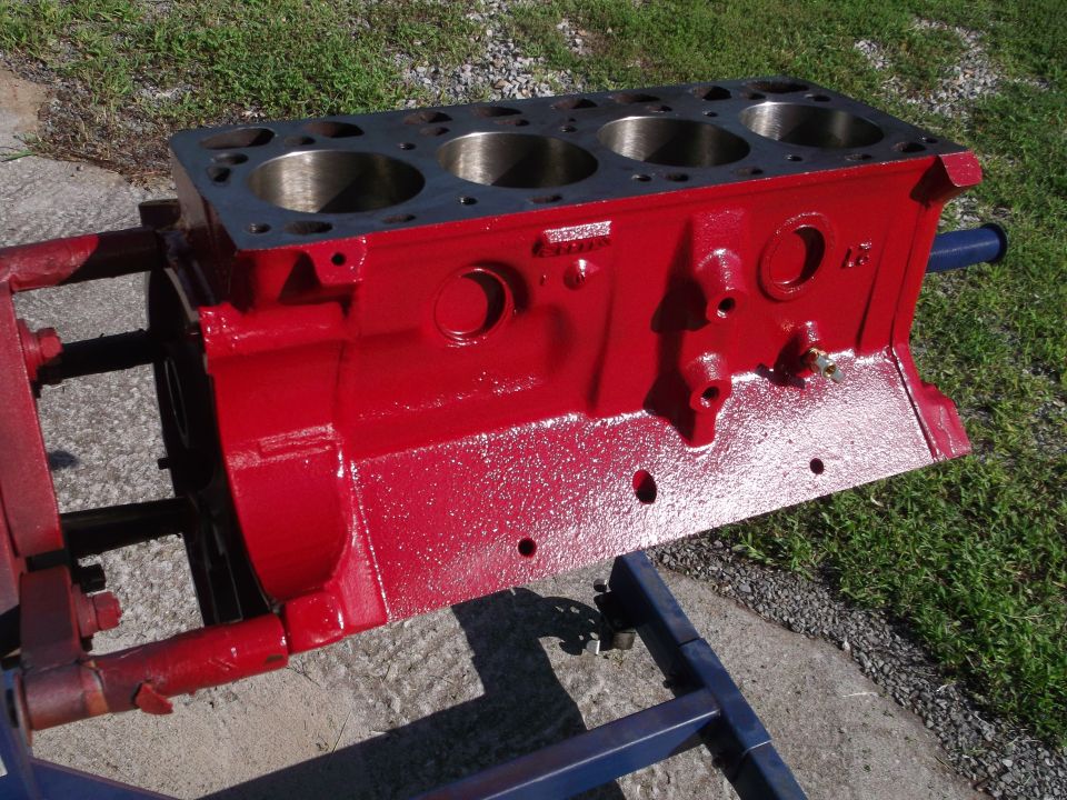 Red painted engine block with four cylinders visible, mounted on a blue and red stand outdoors