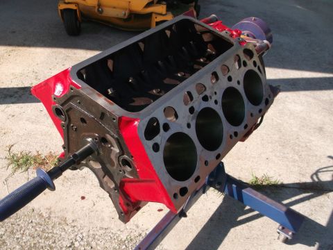 1957 Ford Custom Sedan - A red and gray engine block is mounted on a blue stand outdoors, with a lawnmower visible behind it.