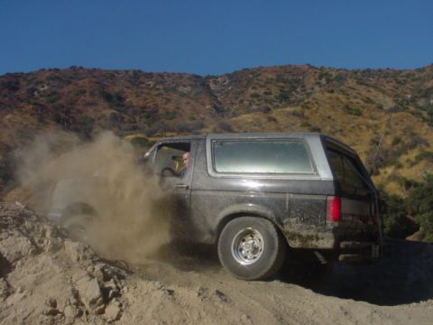 1988 Ford Bronco - A Ford Bronco navigates a dusty, off-road trail under a clear blue sky.