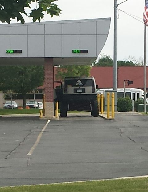 1995 Ford Bronco - SUV with large tires is parked at a drive-thru window, with yellow bollards nearby.