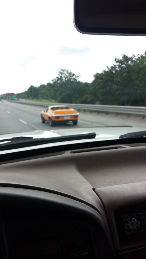 1995 Ford Bronco - An orange sports car is seen from the perspective of another vehicle on a highway.