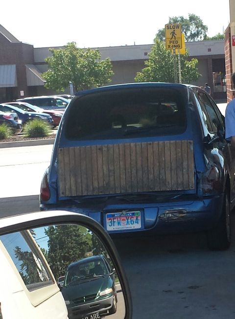 1995 Ford Bronco - A blue hatchback with a custom wooden panel covering its rear hatch is seen at a gas station.