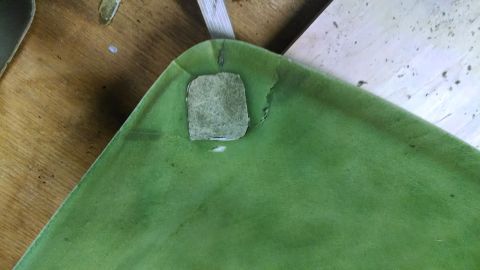 1992 Ford Bronco - A close-up view of a damaged green automotive headliner, revealing exposed material and frayed edges.