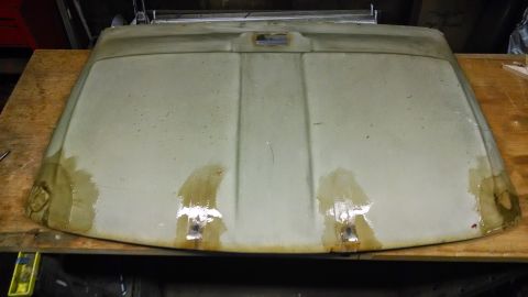 1992 Ford Bronco - The underside of a light-colored, possibly beige, car headliner is shown resting on a wooden workbench. The headliner has visible water sta…