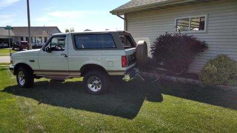 1994 Ford Bronco - A white 1994 Ford Bronco is parked on a grassy lawn next to a house. The vehicle is viewed from the rear quarter angle, showing its side pr…