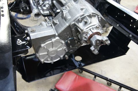 1979 Ford Bronco - A close-up view of a transfer case assembly, likely from a 1979 Ford Bronco, mounted on a black metal bracket. The transfer case is silver…