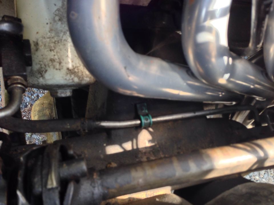 Close-up of engine bay with exhaust headers and a green hose clamp.