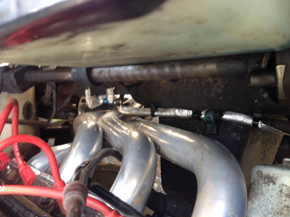 Chrome exhaust manifold and red spark plug wires with a silver insulated hose on a vehicle engine.