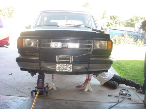 1988 Ford Bronco - A black Ford Bronco is lifted on jack stands for repairs, showing its front end with a winch and bumper.