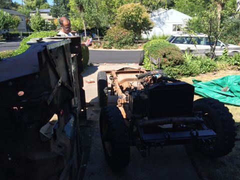 1946 Jeep Willys - A man is working on a vintage Jeep chassis, which is partially disassembled. Another vehicle chassis is visible to the left, and a white se…