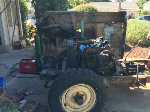1946 Jeep Willys - A partially disassembled vintage Jeep chassis is in a driveway, with a welding machine and a gas cylinder nearby. The engine and drivetrain…