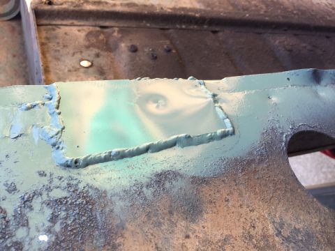 1946 Jeep Willys - A close-up view shows a patch welded onto a metal surface, covered in a light green primer. The welds are rough and visible, with some text…