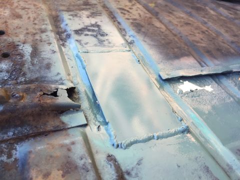 1946 Jeep Willys - A close-up view of a rusty metal surface, likely a vehicle floor pan, showing areas of repair with new metal patches and welds covered in a…