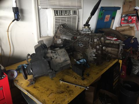 1994 Ford Bronco - A disassembled transmission and transfer case are laid out on a yellow workbench. The transmission is large and appears to be heavily used,…