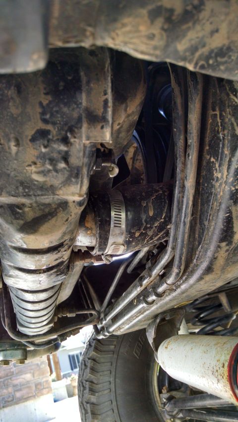 1979 Ford F-150 - The underside of a vehicle shows a black hose with a metal clamp connecting two sections. Several metal lines and suspension components are…