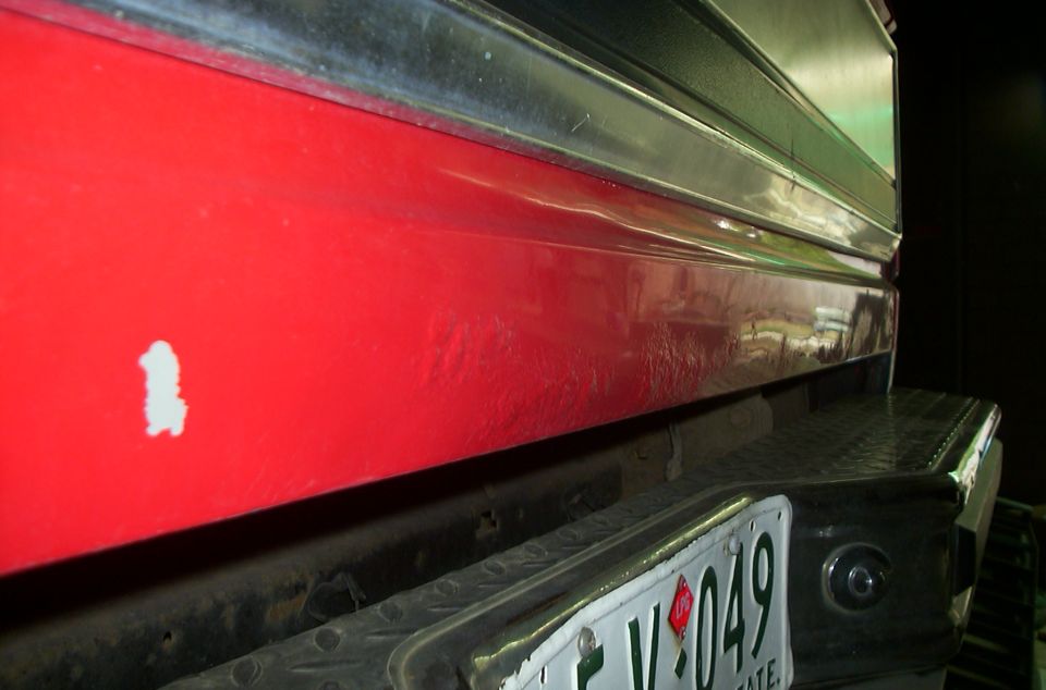 Close-up of red Bronco tailgate with chrome trim, paint chip, diamond-plate bumper, and partial license plate