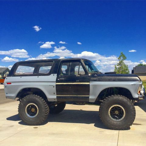 1979 Ford Bronco - A lifted 1979 Ford Bronco with a two-tone black and gray paint scheme sits parked on a concrete driveway under a bright blue sky with scatt…