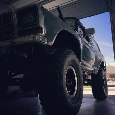 1979 Ford Bronco - Low-angle shot of a lifted, dark-colored Ford Bronco parked inside a garage with the door open. The front of the vehicle is visible, featur…