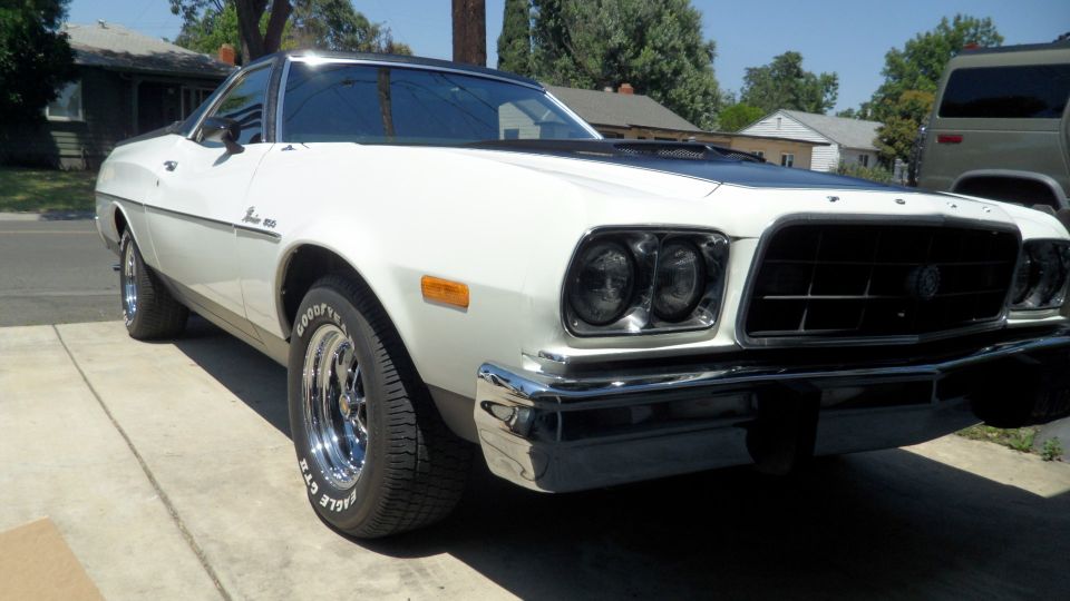 White 1973 Ford Ranchero with chrome wheels and black hood stripe parked on a driveway.