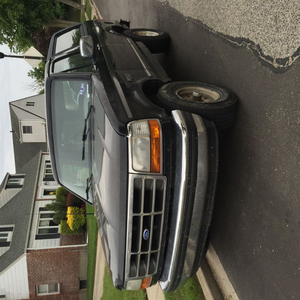 Dark-colored Ford Bronco parked on a residential street, front 3/4 view.