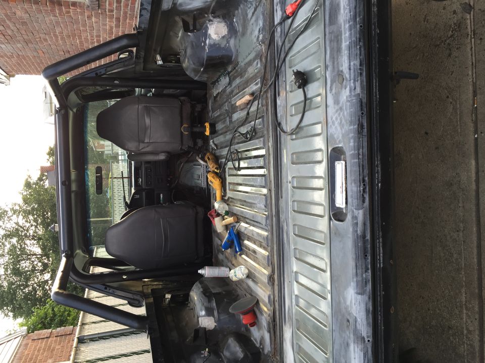 Interior and bed of a black SUV with roll cage, seats, and tools.