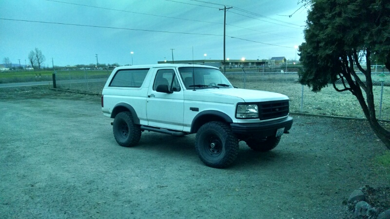 White two-door Ford Bronco with large off-road tires parked on a gravel lot.