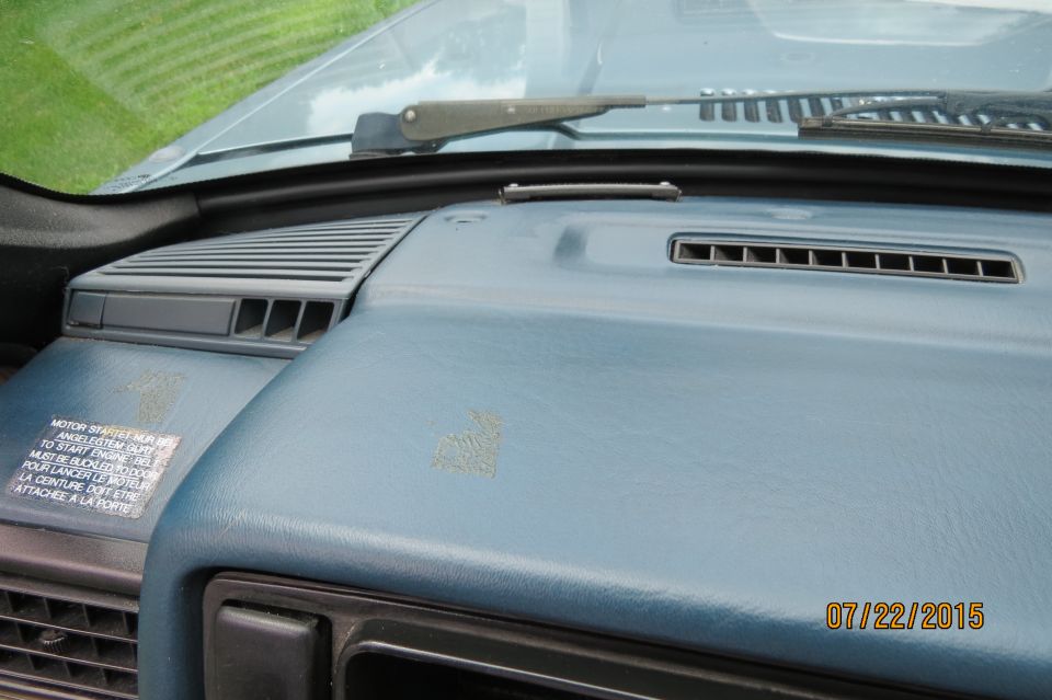 Interior dashboard of a light blue car with air vents and a sticker.